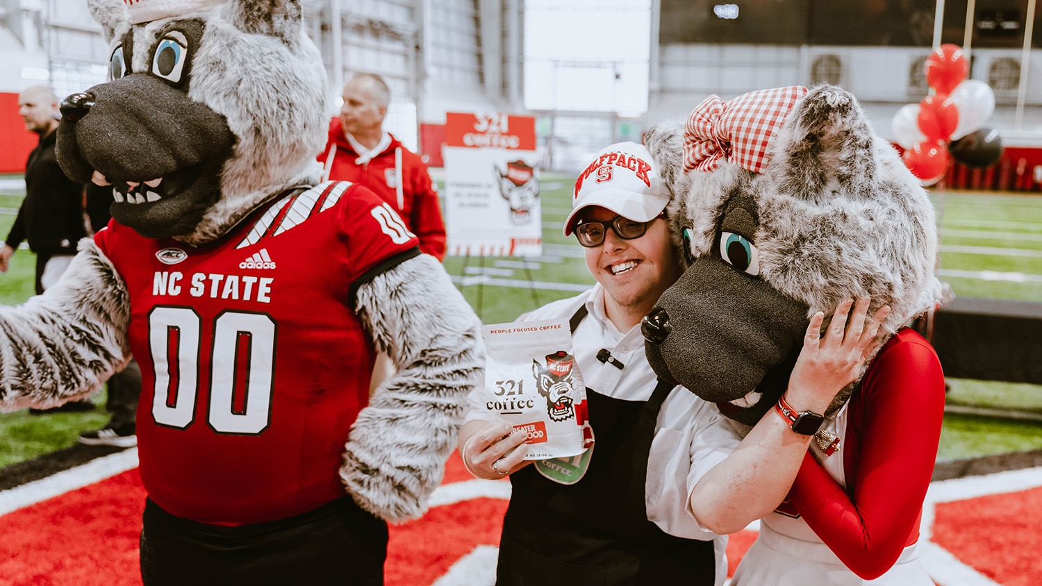 Sam, a 321 Coffee employee, hugs Ms. Wuf while holding a bag of the company's new NC State co-branded Greater Good coffee.