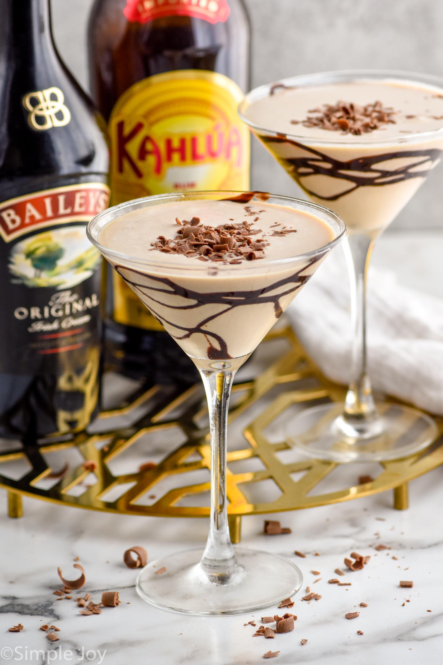 martini glass of Mudslide topped with chocolate shavings. Glass of mudslide, bottle of bailey's irish cream, and bottle of kahlua sitting in background