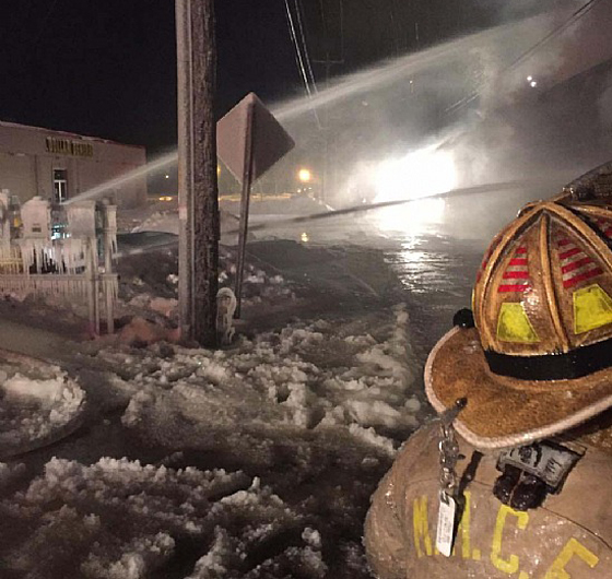 Firefighter at icy nighttime scene with water spraying.