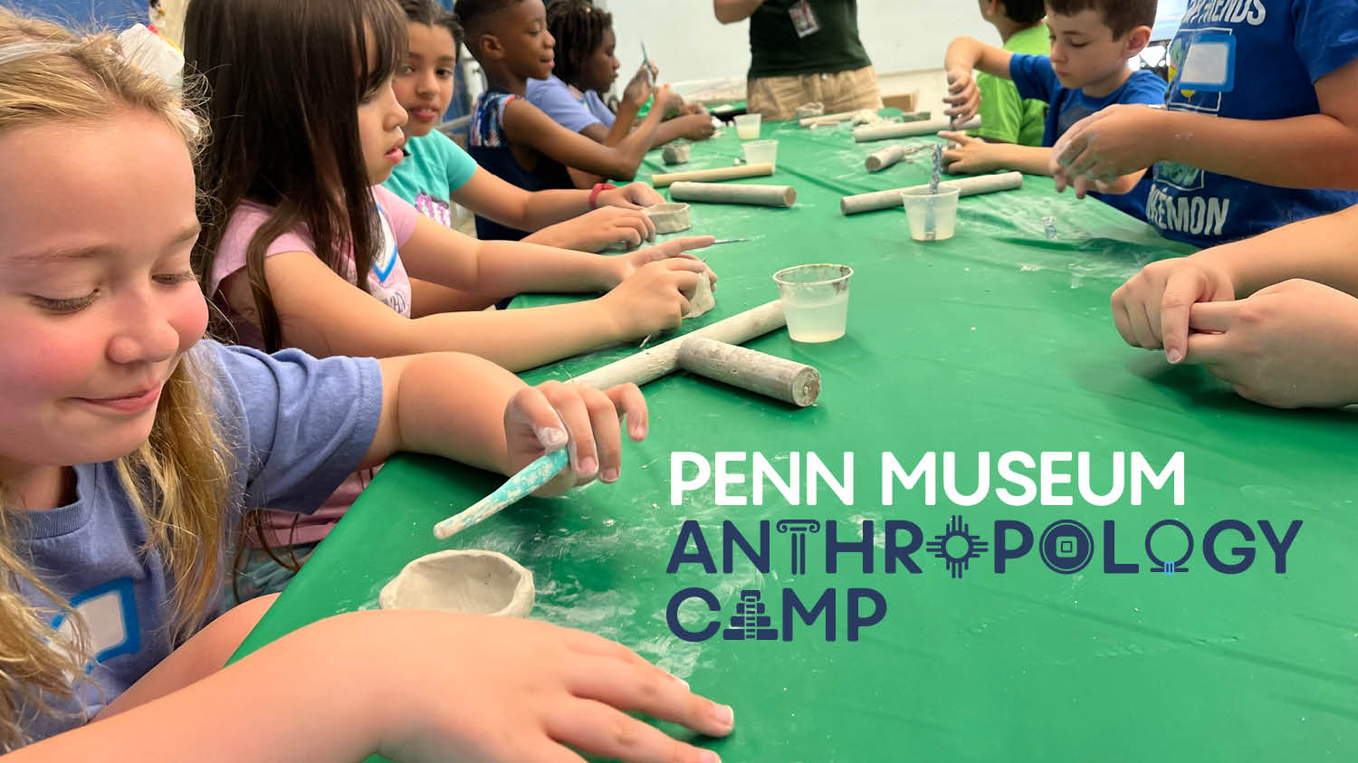 The Penn Museum Anthropology Camp 2023 logo over a photo of campers doing crafts at a table.