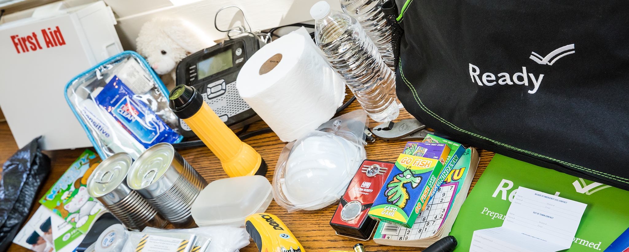 The items  in an emergency supply kit spread out on a table including water bottles, toilet paper, and batteries