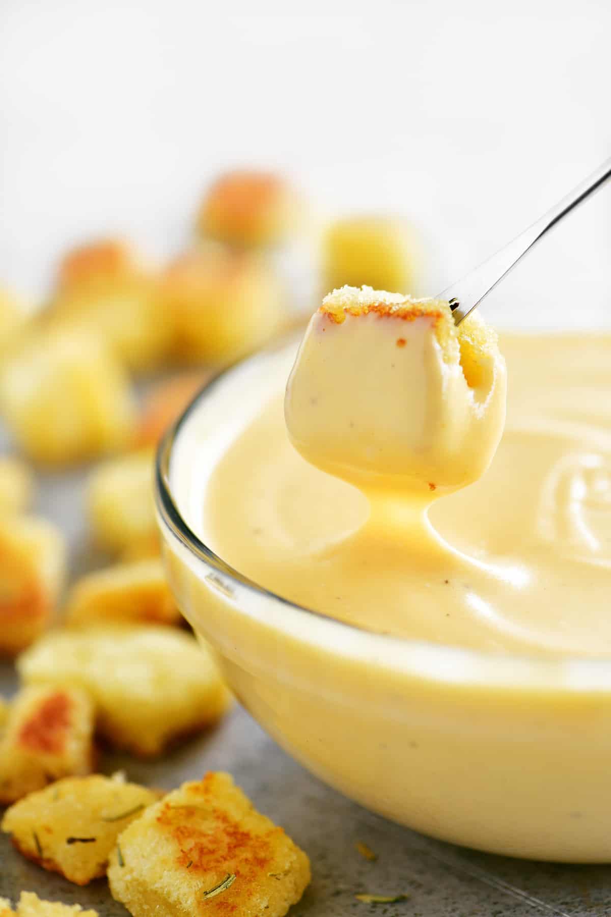 dipping a golden crouton into creamy cheese sauce