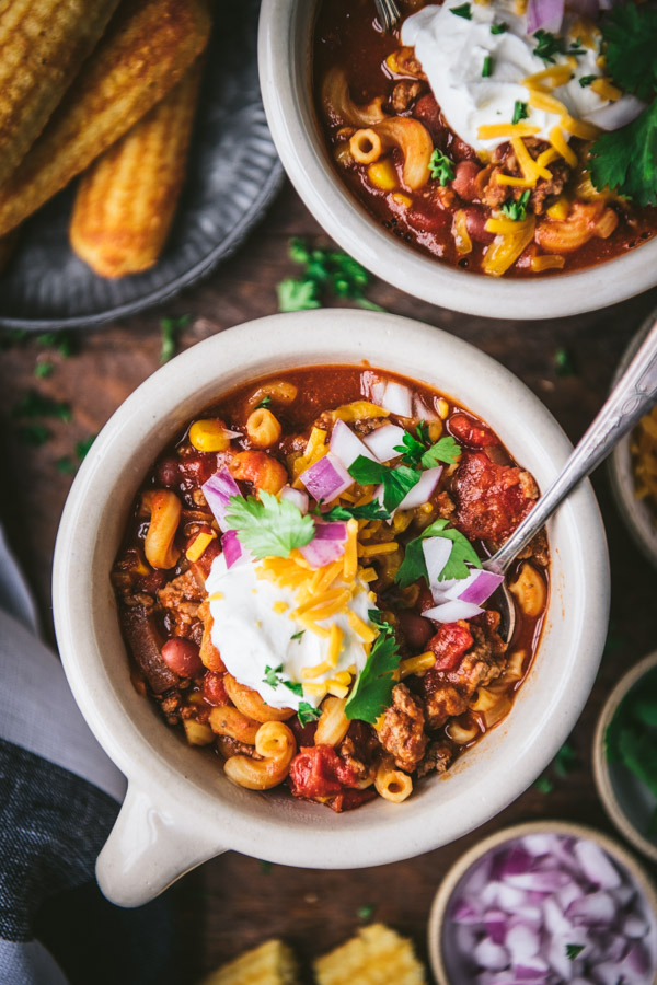 Overhead image of a bowl of chili mac on a dinner table with cornbread