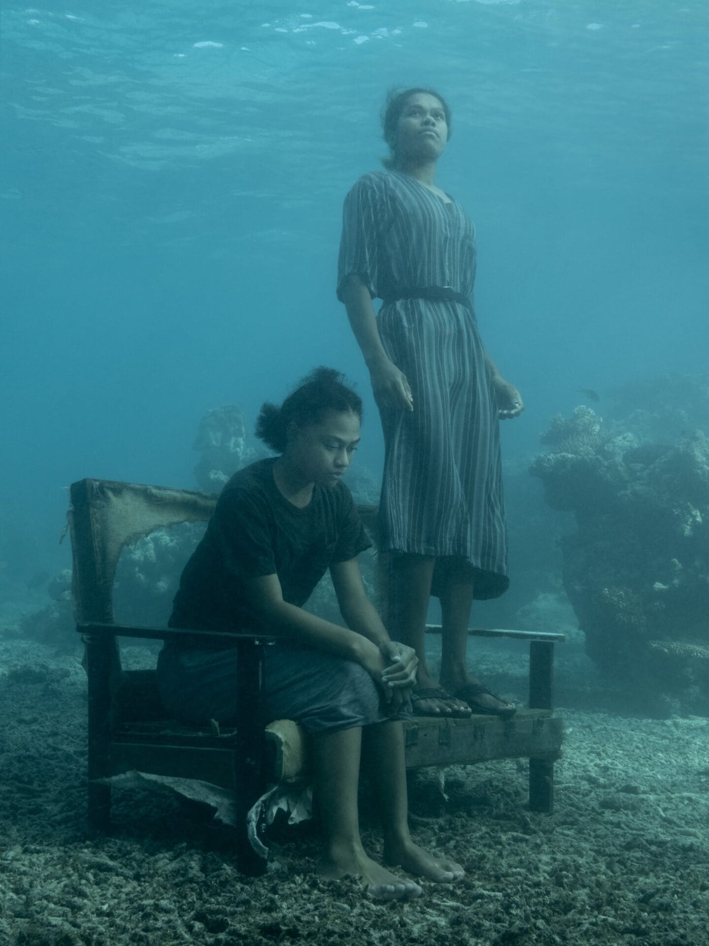 two young women, one sitting on a bench and the other standing on it at the bottom of the ocean floor