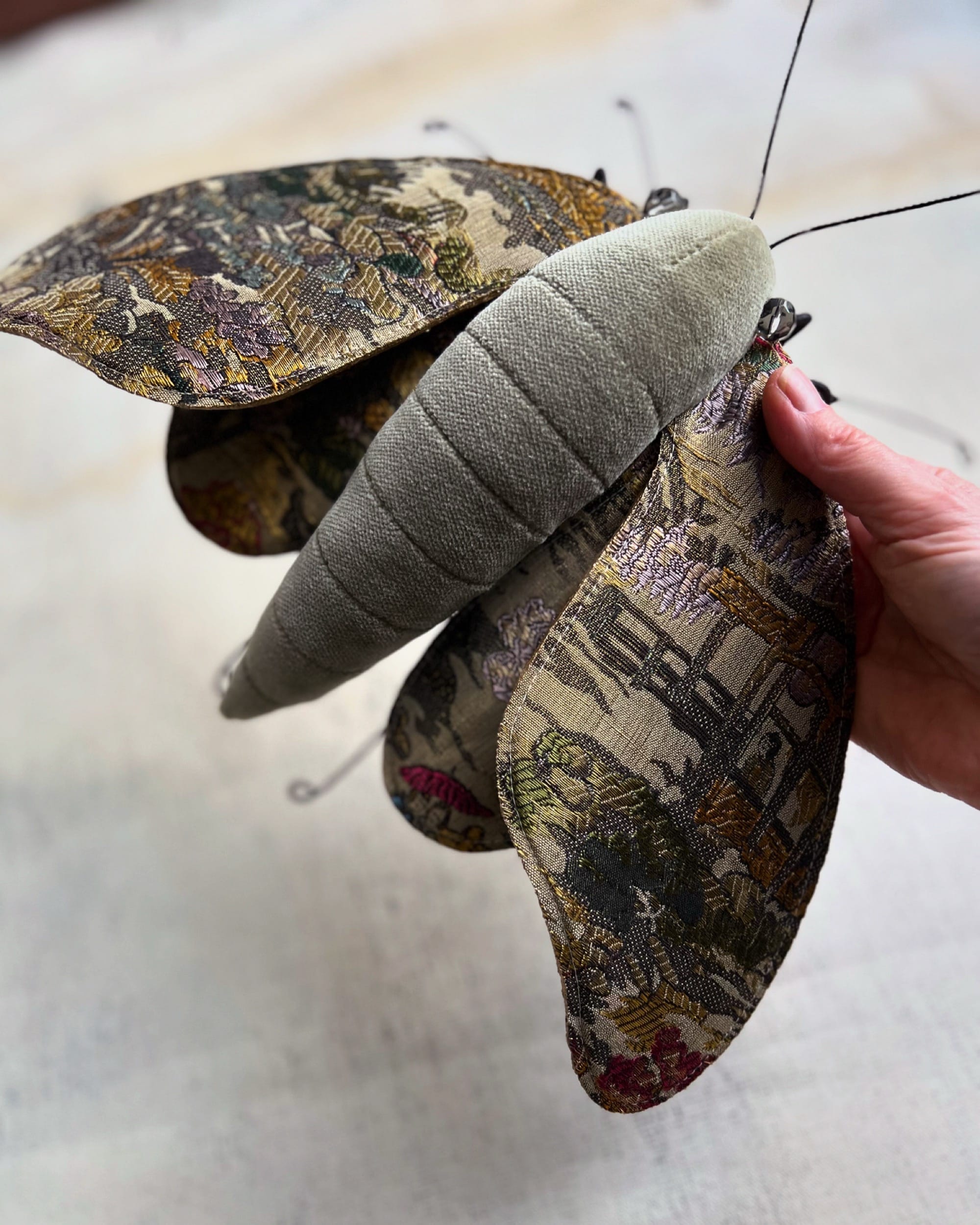 a hand holds a moth sculpture made from textile and wire