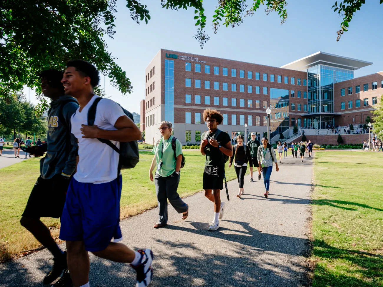 Diverse students walking across the campus green, the new University Hall behind them.