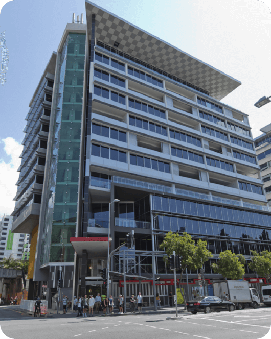 Office building with a glass front on a tree-lined street with vehicles and pedestrians on the road