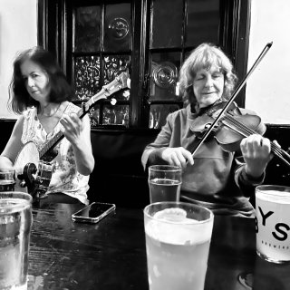 A woman playing banjo next to a woman playing fiddle at a pub table.