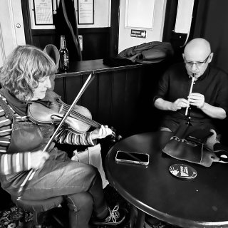 A woman playing fiddle and a man playing tin whistle at a small round table.