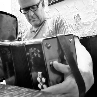 Close up of a button accordion being played at a pub table by a man wearing glasses.