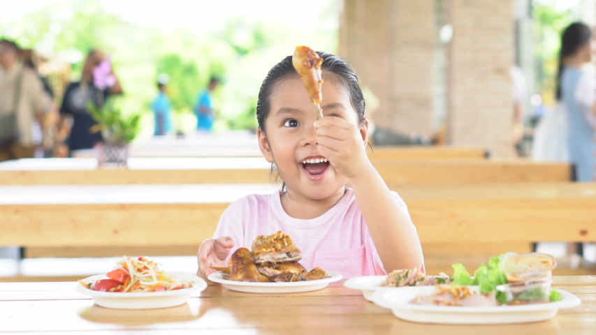 Asian child cute or kid girl enjoy eating grilled chicken and papaya salad for Thai food and appetizing on table with smiling and happy for breakfast or lunch in restaurant or food court on slow