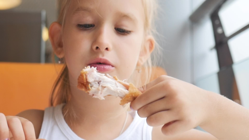 Beautiful young girl eating chicken in the cafe. The child greedily eating chicken, fat and delicious, very hungry.