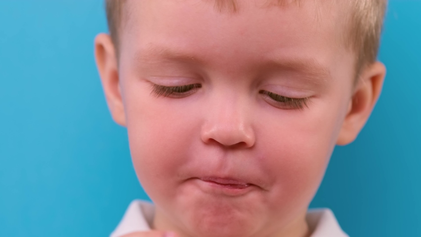 Portrait of child eating chicken nuggets, chicken leg, chicken fillet from fast food restaurant on blue background. Blond caucasian boy eats deep-fried chicken leg close-up.