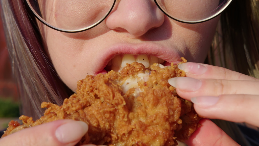 Young woman with glasses eating fried chicken . Fast food concept. Close up