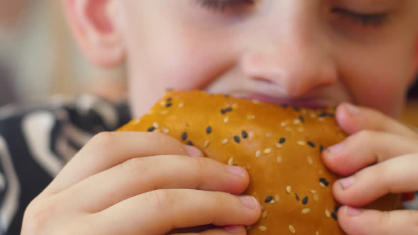 Close-up european boy eats a big burger in a cafe. selective focus. fast food concept, children eat burgers