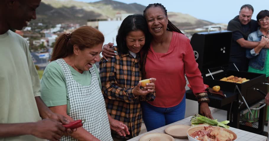 Multi generational people doing barbecue during weekend day at home's rooftop preparing food - Multiracial friends having fun smiling in front of camera