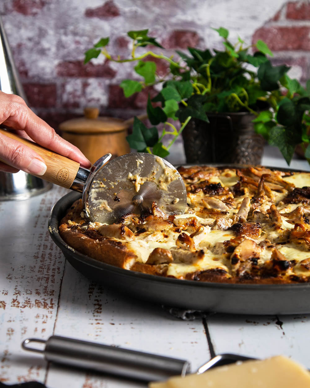 Side view slicing a Jamaican jerk chicken pizza on a white counter with red brick background