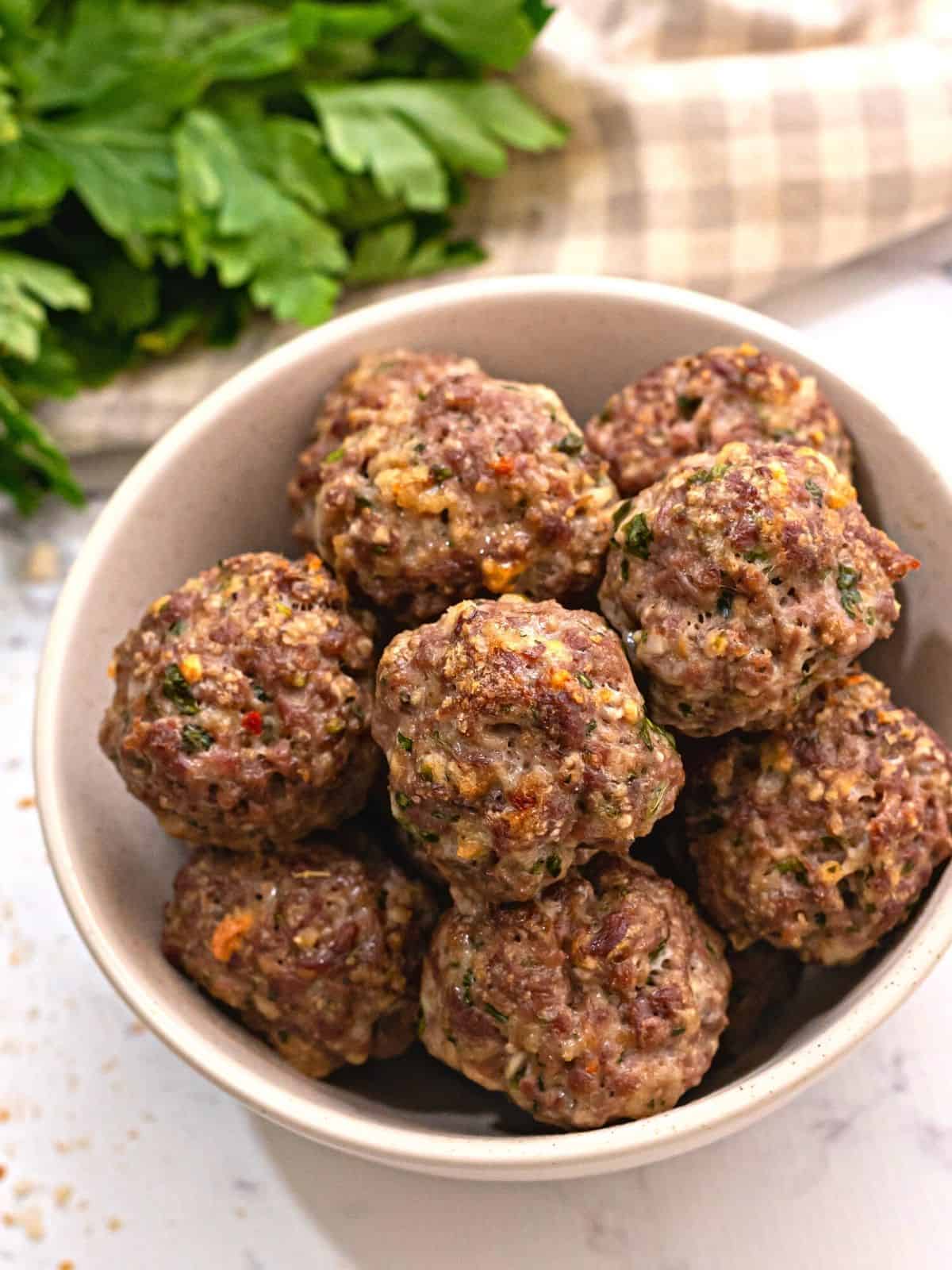 Italian seasoned baked meatballs in bowl next to fresh parsley.