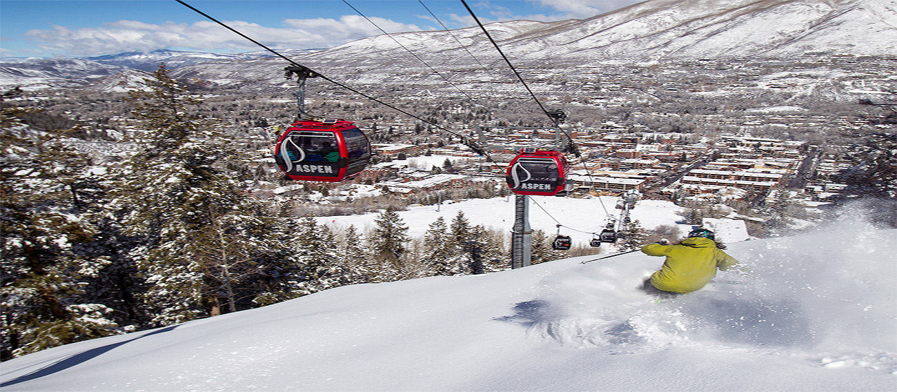 Man skiing fresh powder under Aspen Mountain Gondola in Aspen, Colorado during peak winter season