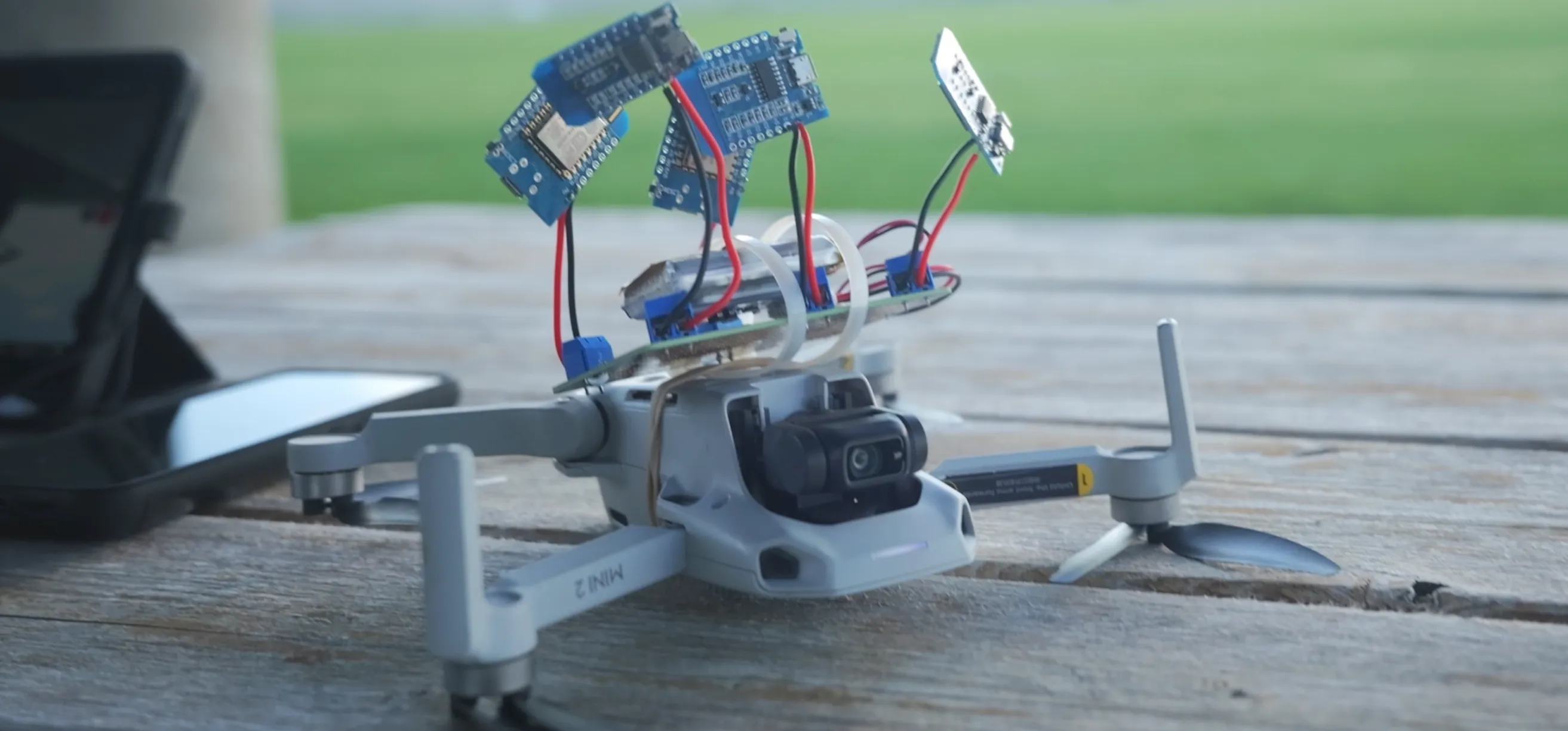 A DJI 2 mini quadcopter drone on a picnic table, equipped with D1 Mini microcontrollers powered by a LiPo battery pack.