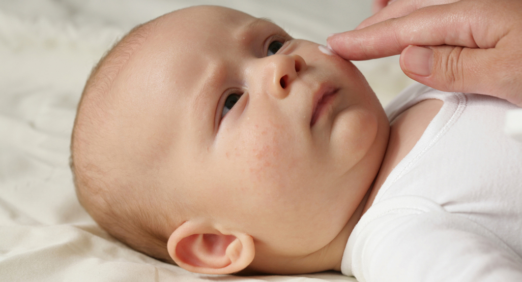 person gently applying face cream to baby's face