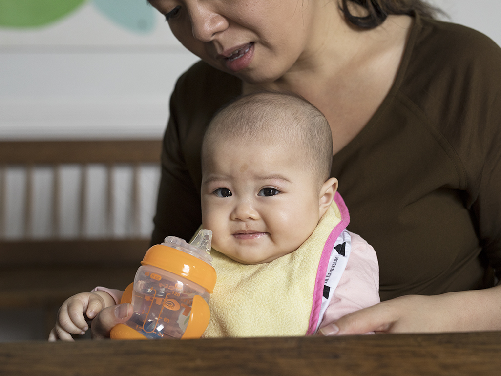 A baby drinking water from a sippy cup while sitting in a woman's lap