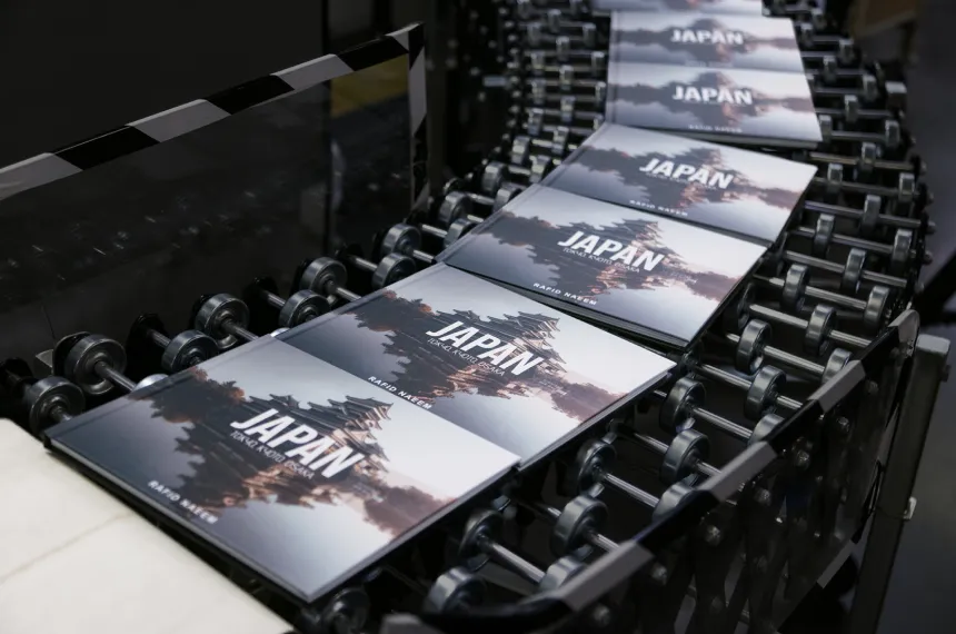 Freshly printed books on a conveyor belt in a print production facility, featuring a Japanese building on the cover.