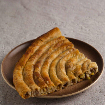 Quarter of a burek pie on a plate on gray background.