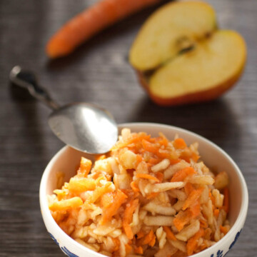 Bowl with carrots and apple, and carrot and apple and a spoon on a table.