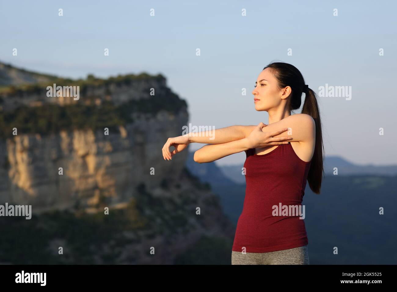 Asian sportswoman stretching arms in the mountain at sunset Stock Photo