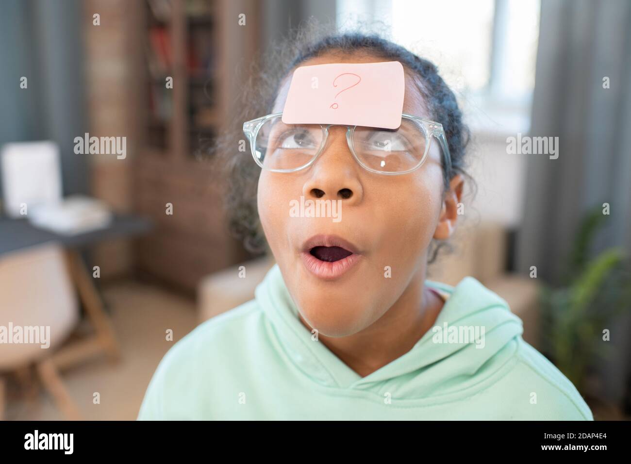 Girl in eyeglasses looking at notepaper with question mark on her forehead Stock Photo