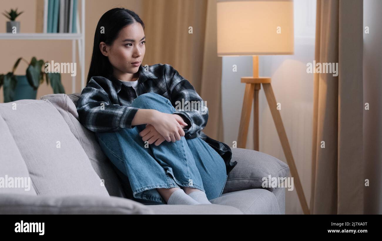 Alone offended sad thoughtful Asian woman upset frustrated girl looking away thinking of problems sitting at home worries troubled negative bad mood Stock Photo