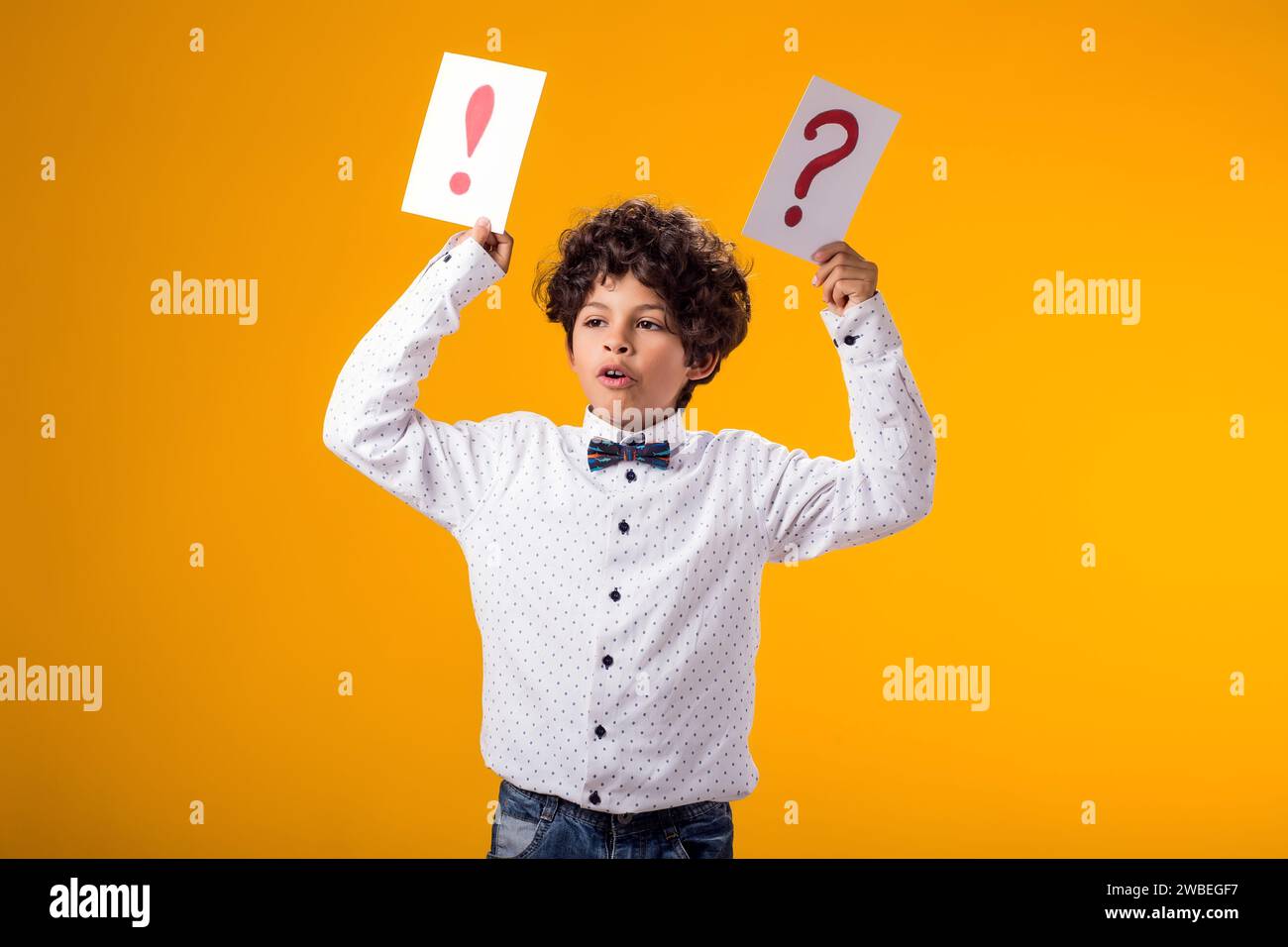 Portrait of child boy holding question mark and exclamation point cards over yellow background. Brainstorming and choice concept Stock Photo