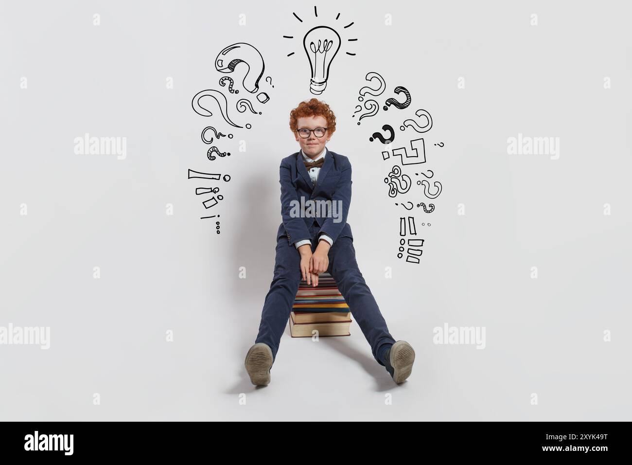 Young child boy in guggles with light bulb and question marks sitting on stack of book on white background. Education and idea concept Stock Photo