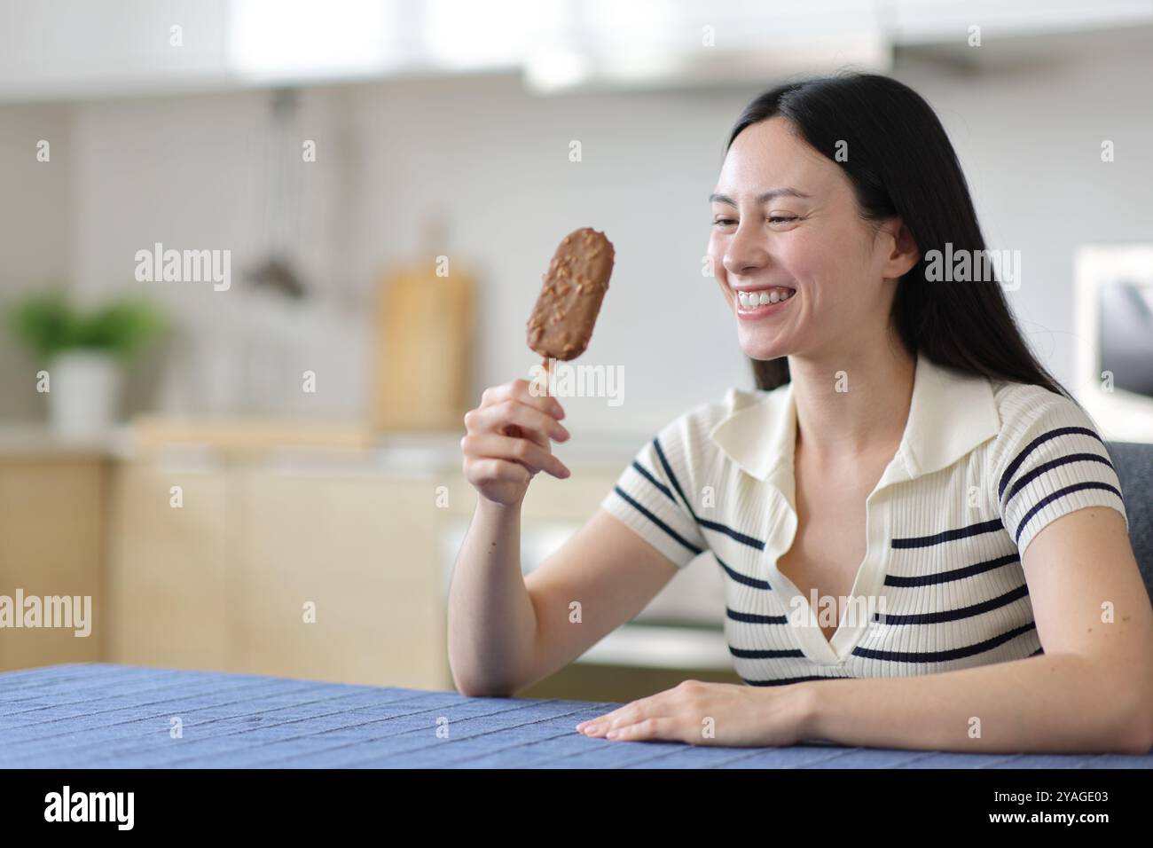 Happy asian woman holding chocolate ice cream and looking it in the kitchen Stock Photo