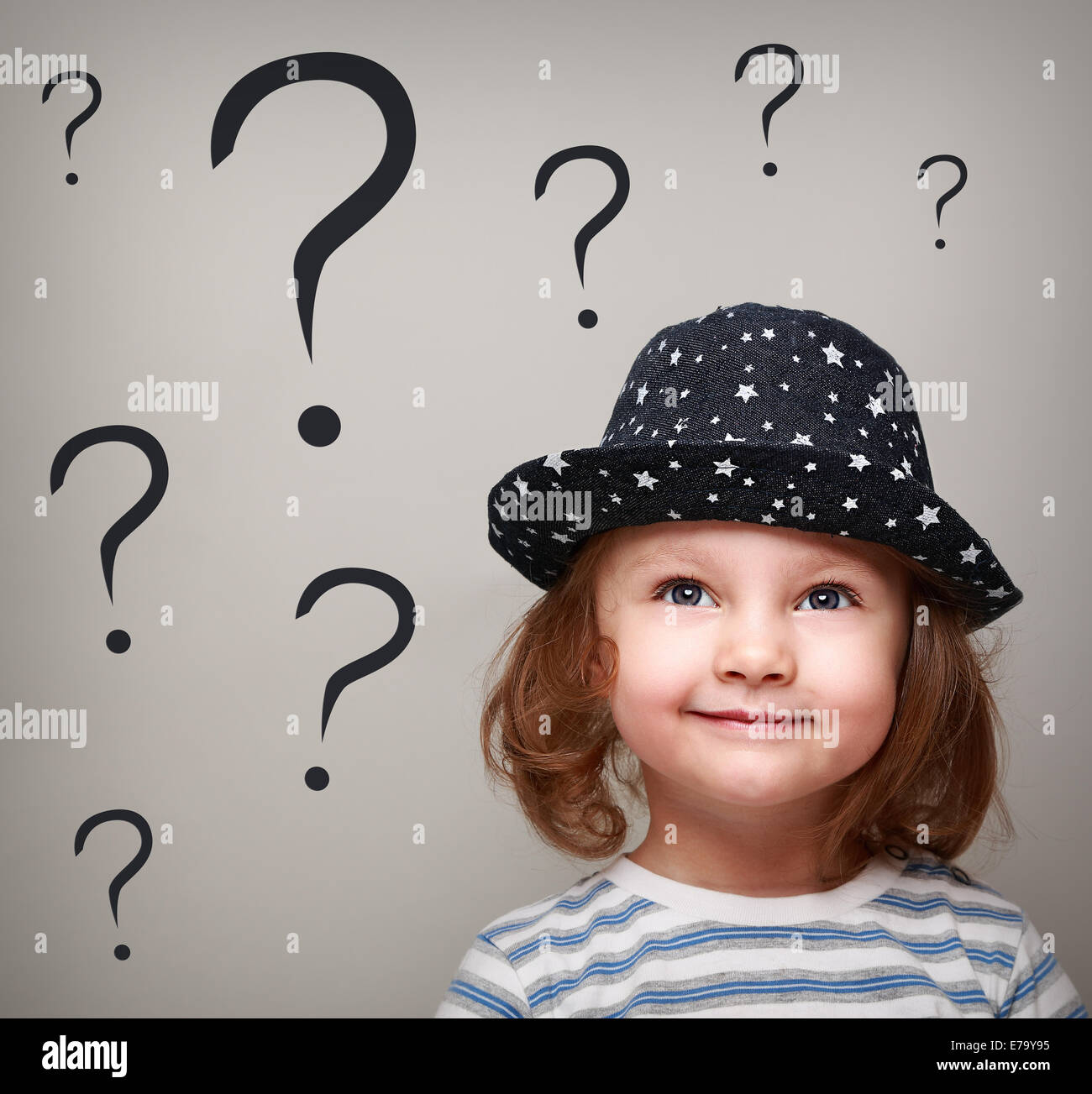 Happy thinking kid girl in hat looking up on many questions above the head Stock Photo