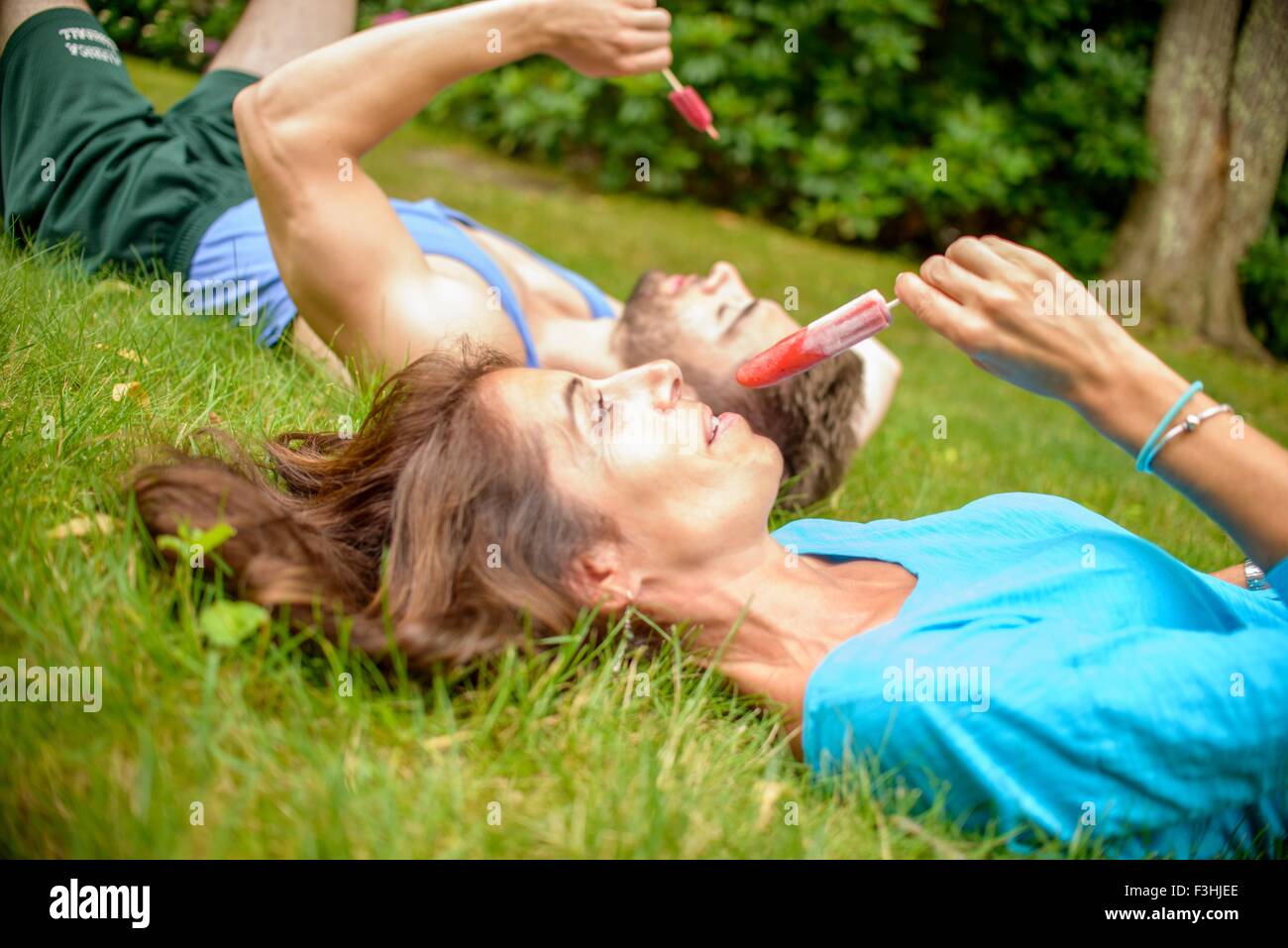 Mature woman and young man lying on grass, eating ice lollies Stock Photo