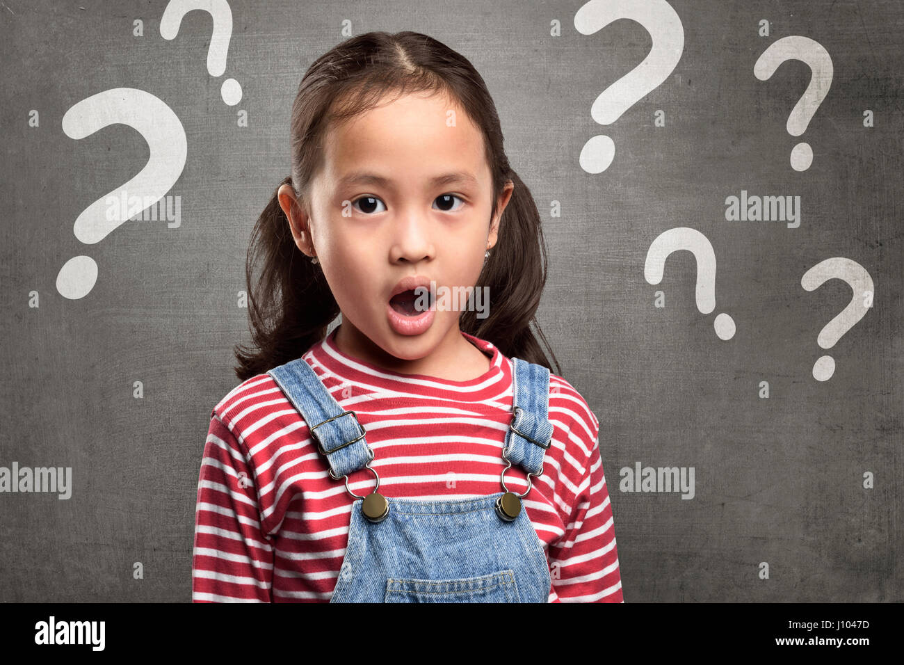 Cheerful asian child expression with question mark above her head over blackboard background Stock Photo