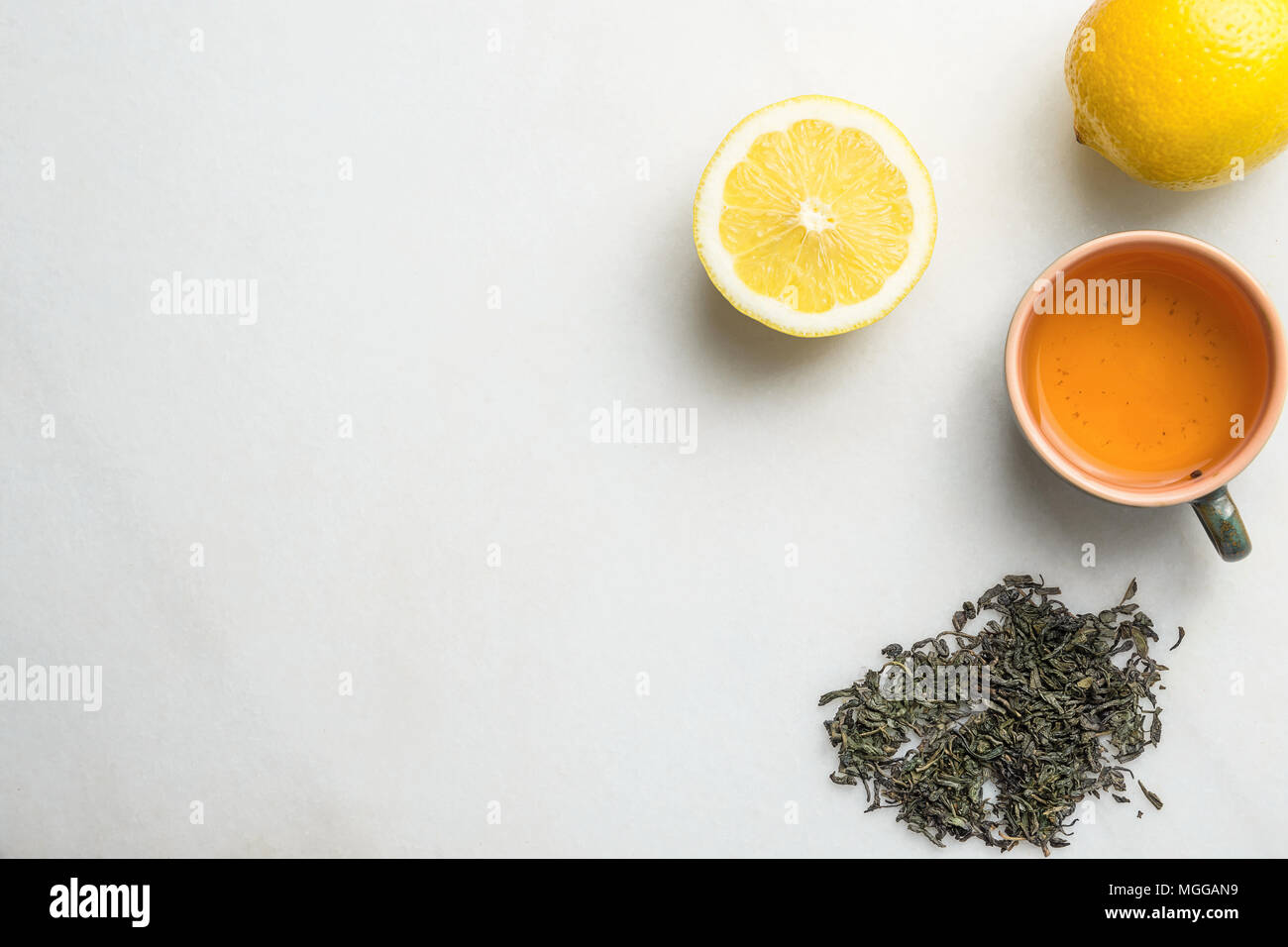 Brewed Green Tea in Ceramic Cup. Loose Leaves Scattered on White Marble Stone Background Slice of Lemon. Chinese Japanese Asian Cuisine. Healthy Drink Stock Photo