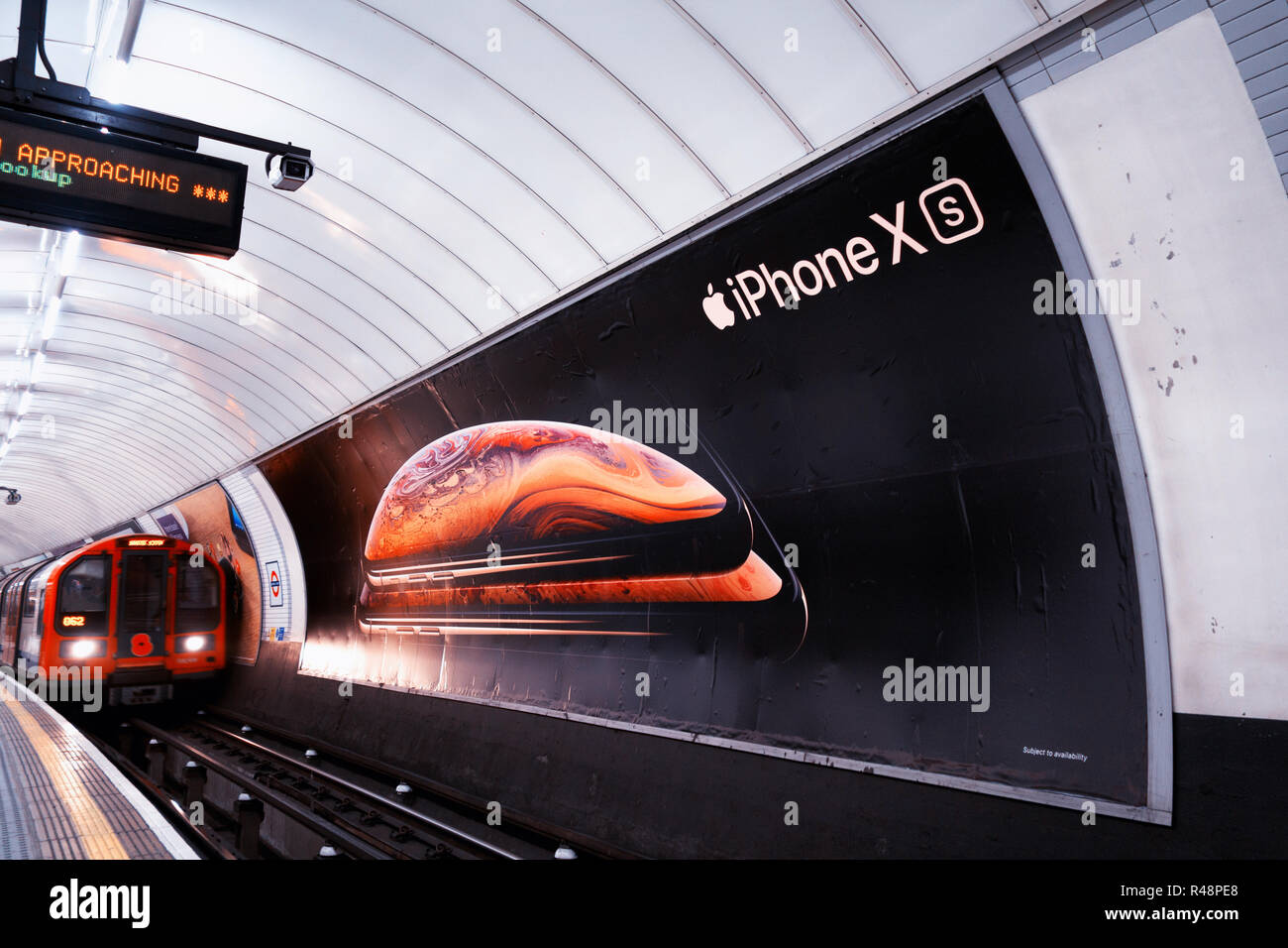 Tube train passing an ad poster for new Apple iPhone XS, advertising poster in the London Underground Track Stock Photo