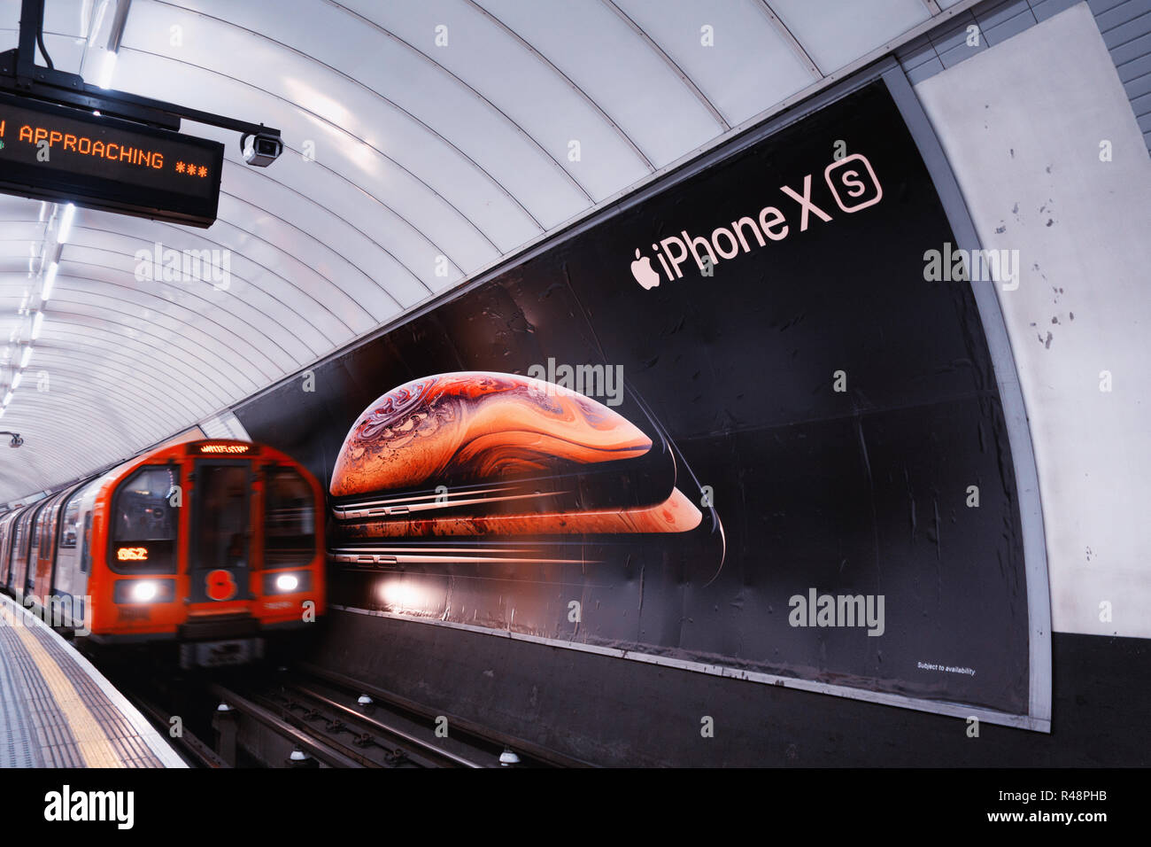 Tube train passing an ad poster for new Apple iPhone XS, advertising poster in the London Underground Track Stock Photo