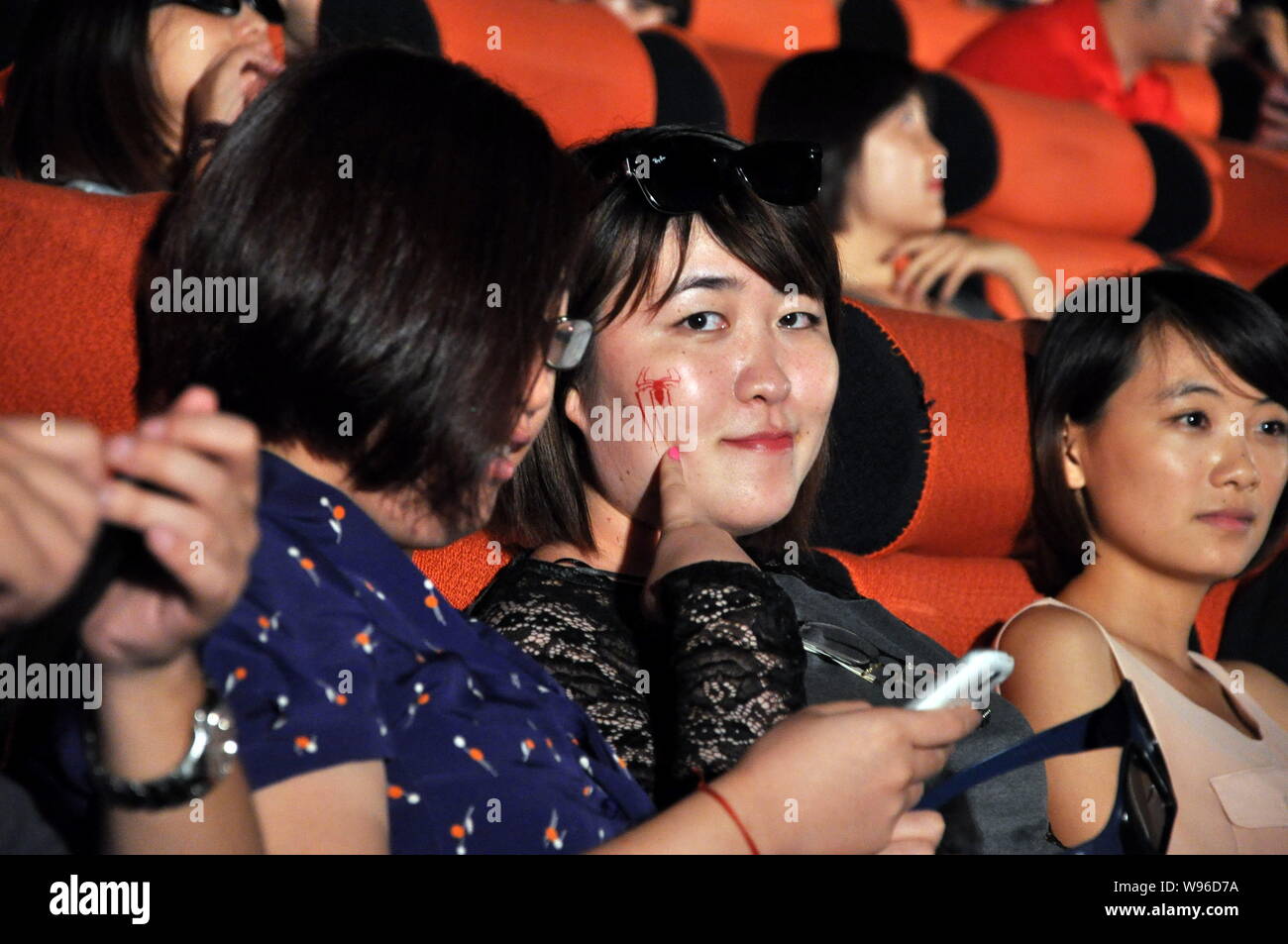 A woman whose face is painted with a spider looks on amongst other audience during the premiere for the movie, The Amazing Spider-man, at a cinema in Stock Photo