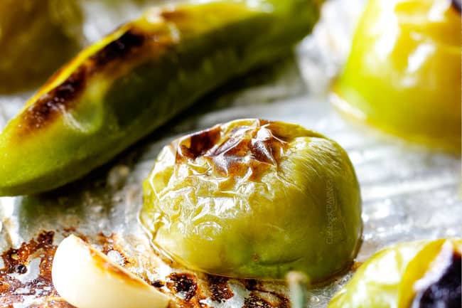 up close of charred tomatillos and serrano peppers on a baking sheet showing how to make homemade salsa verde 