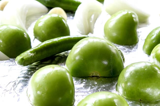 showing how to make homemade salsa verde with a side view of tomatillos, onions and serrano peppers on a baking sheet