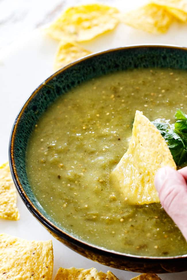 Dipping tortilla chip into a bowl of homemade salsa verde