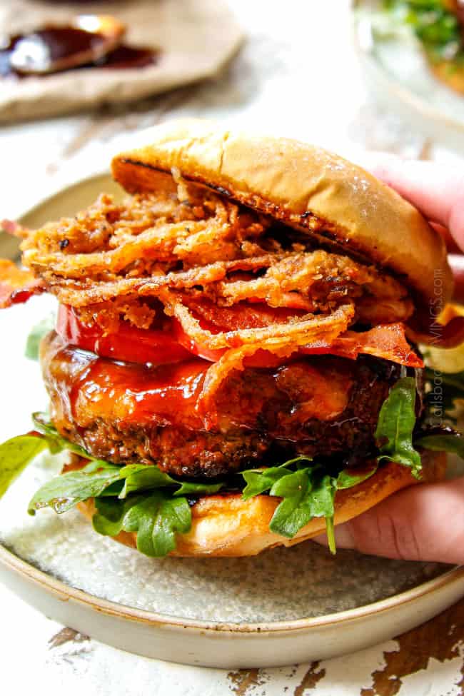 up close showing how to eat BBQ burger recipe with a hand picking up the burger on a plate