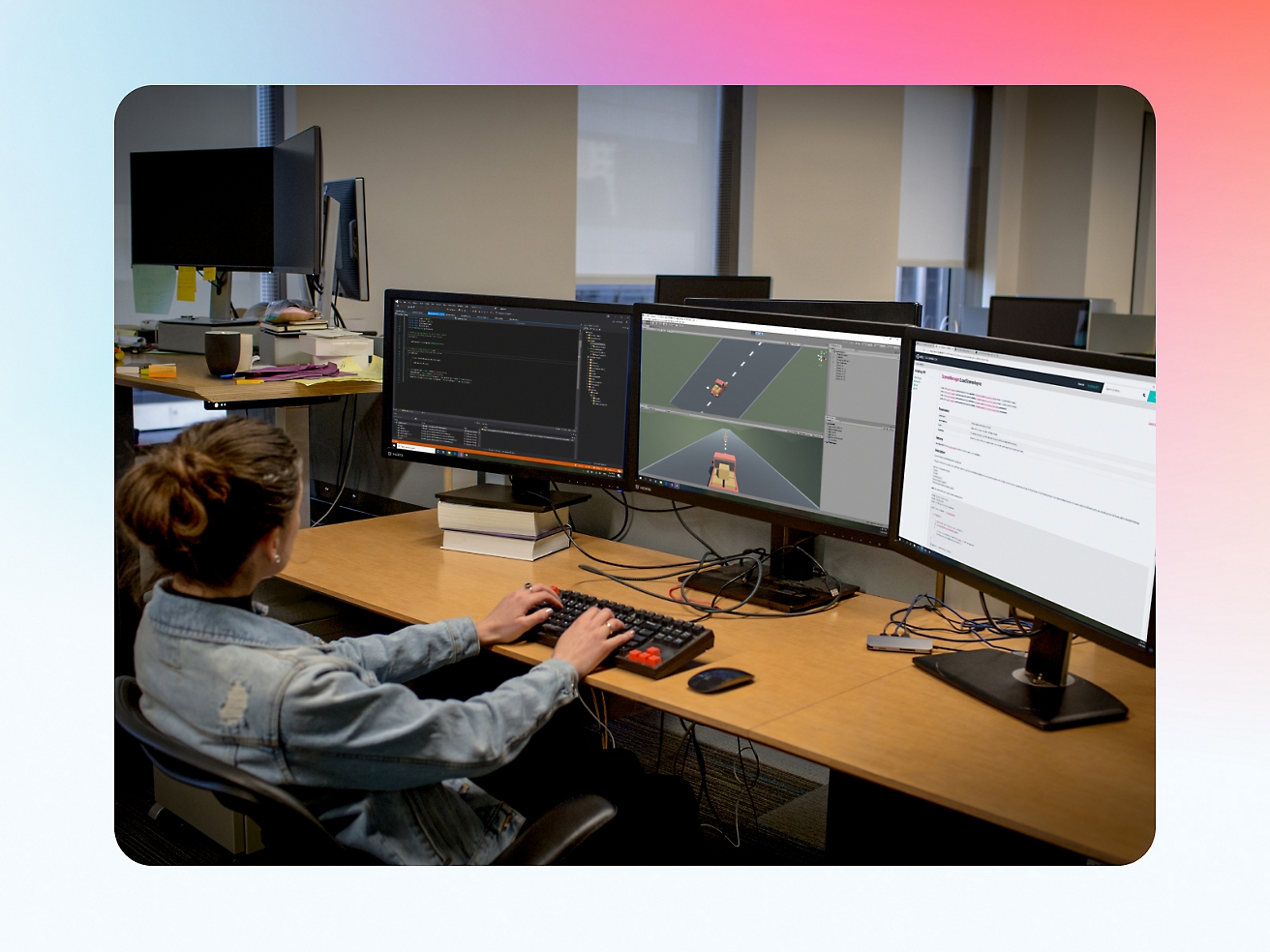 A female software developer working at a multi-monitor setup in an office, coding and debugging software.