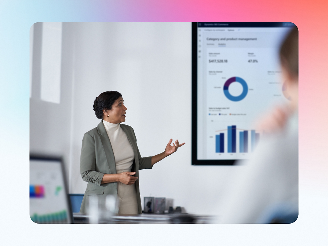 A professional woman presents financial data on a screen to her audience in a modern office setting.