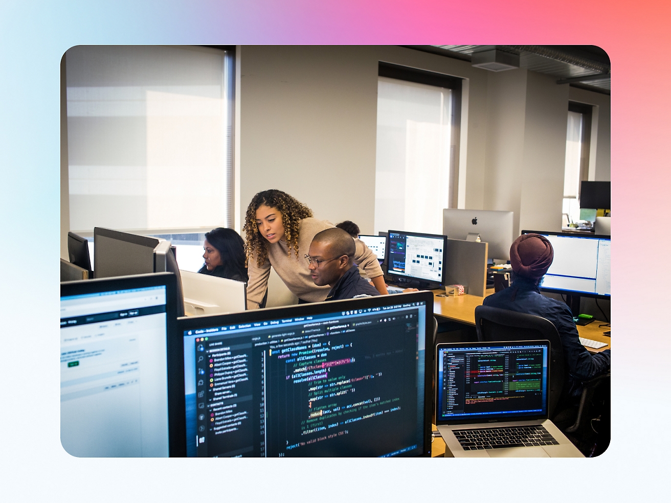 Diverse group of professionals working on computers in an office environment, focusing on screens with various code and data visible.