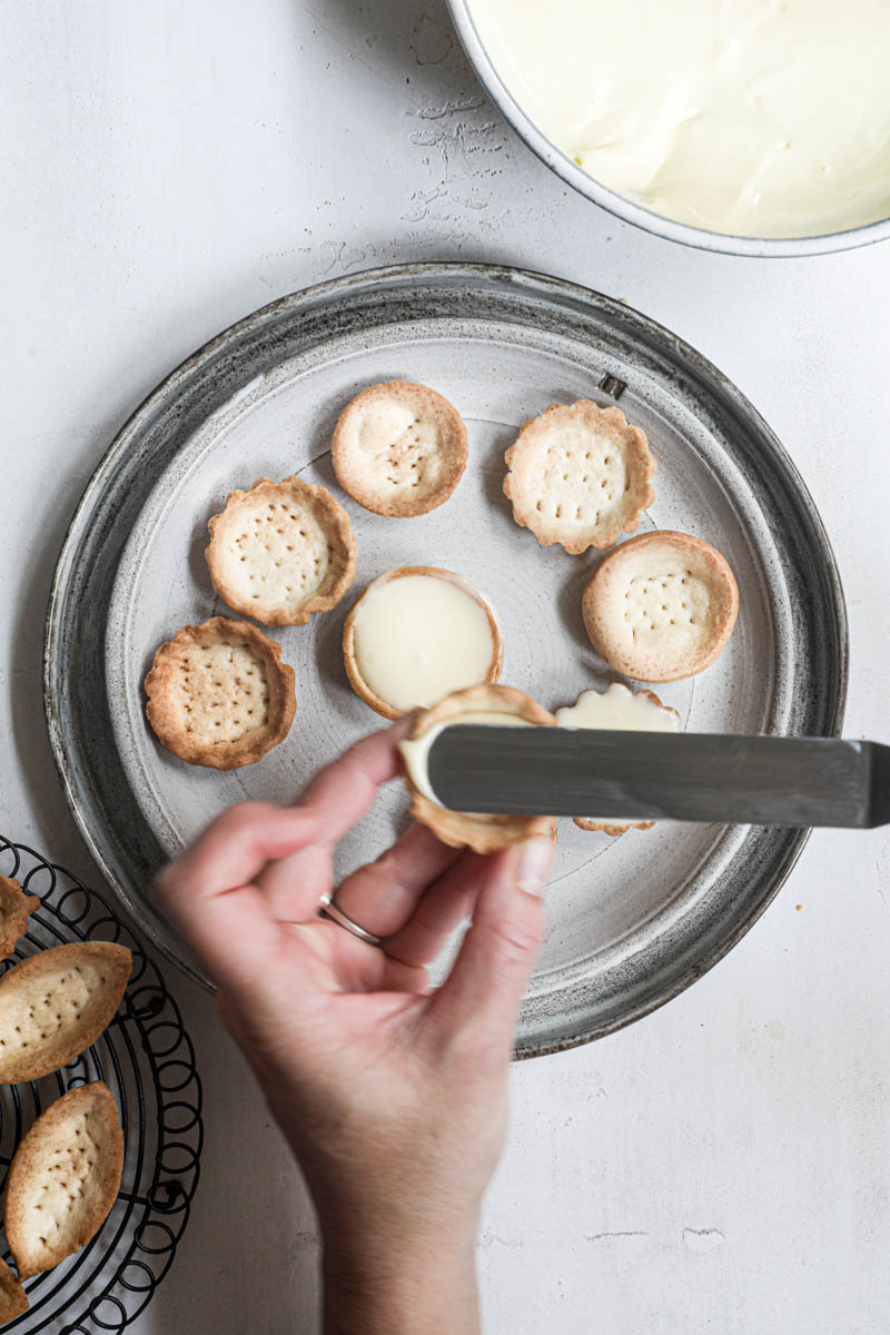 One hand filling the tartlet shells with the lemon cream.